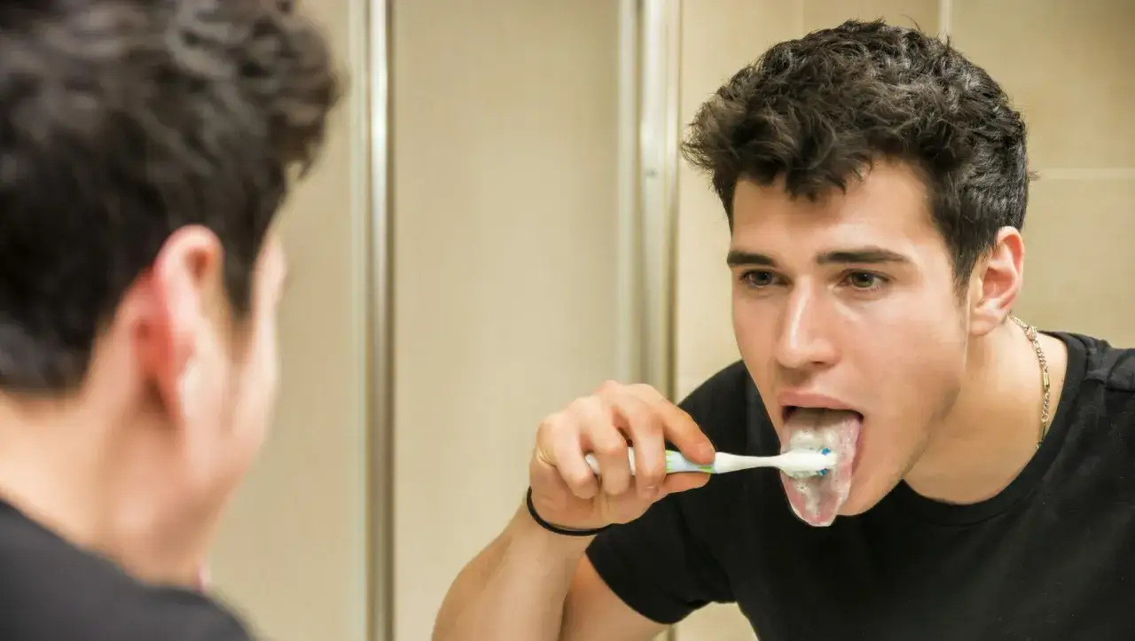 Ragazzo si pulisce la lingua con lo spazzolino, cercando di non vomitare.