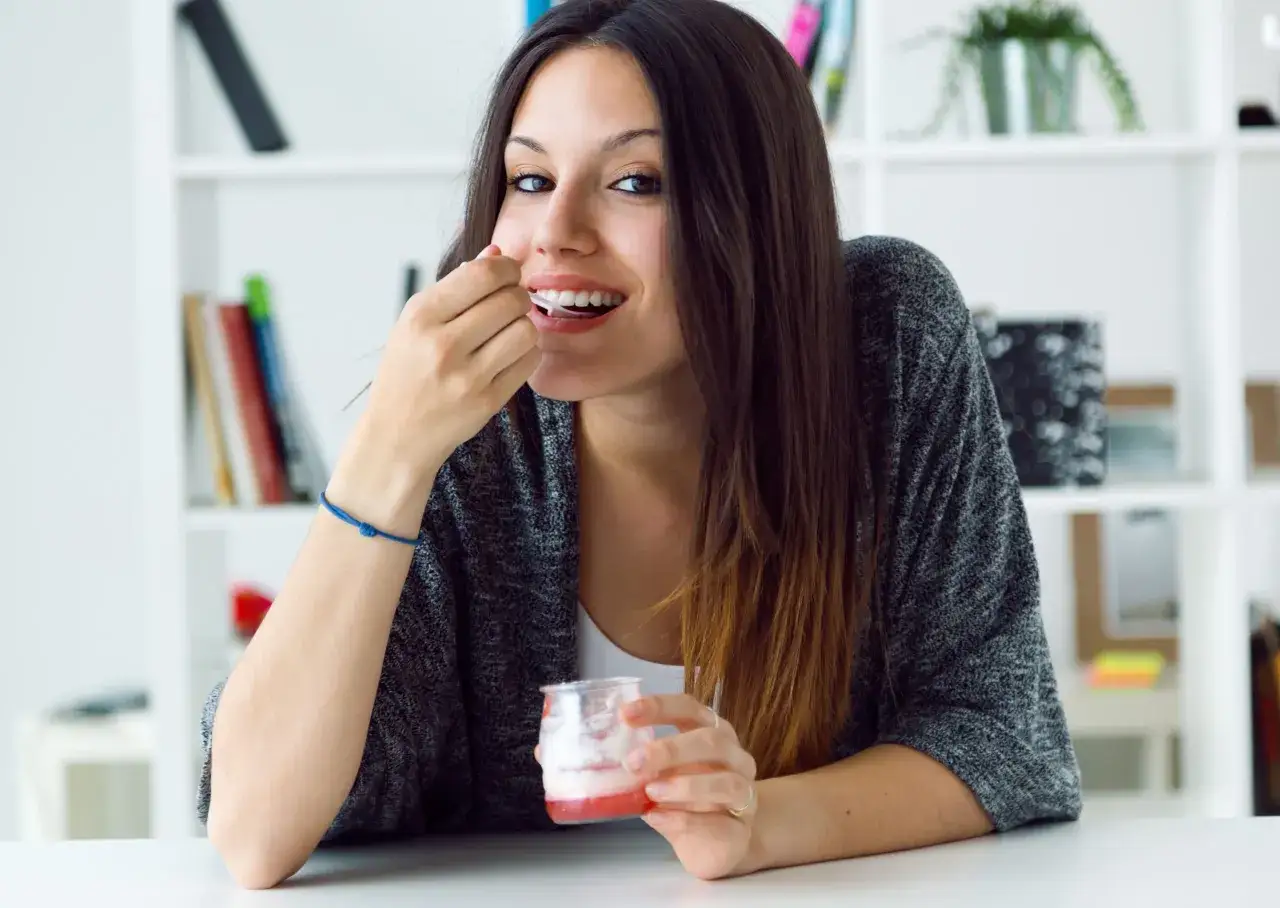 Ragazza sorridente mangia yogurt con Invisalign, godendosi una pausa dolce senza preoccupazioni.
