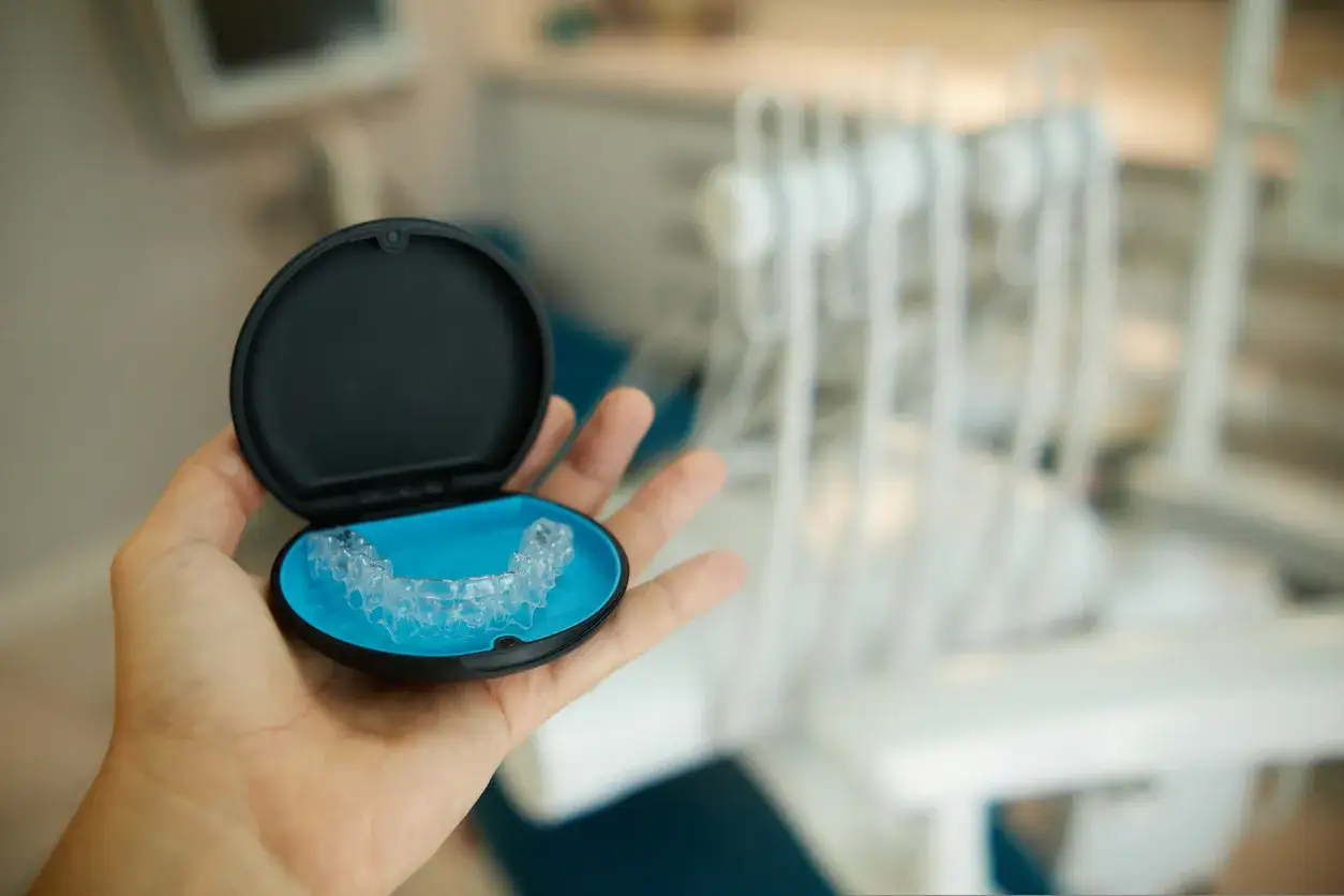 Mano tiene una custodia aperta con allineatori dentali fai da te. Sfondo sfocato di uno studio dentistico.