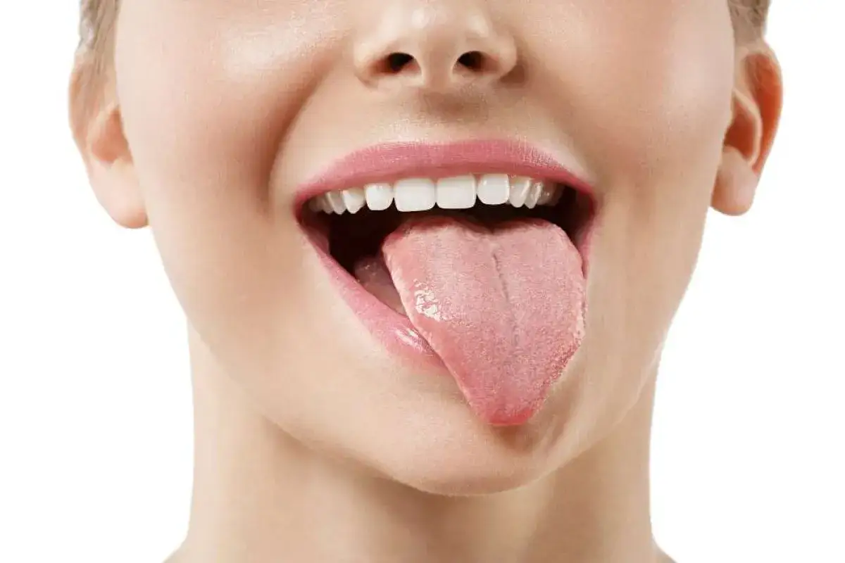 Bocca aperta con lingua rosa estesa, mostrando denti bianchi e labbra lucide. Un rimedio naturale per la pulizia della lingua: sciacqui con bicarbonato.