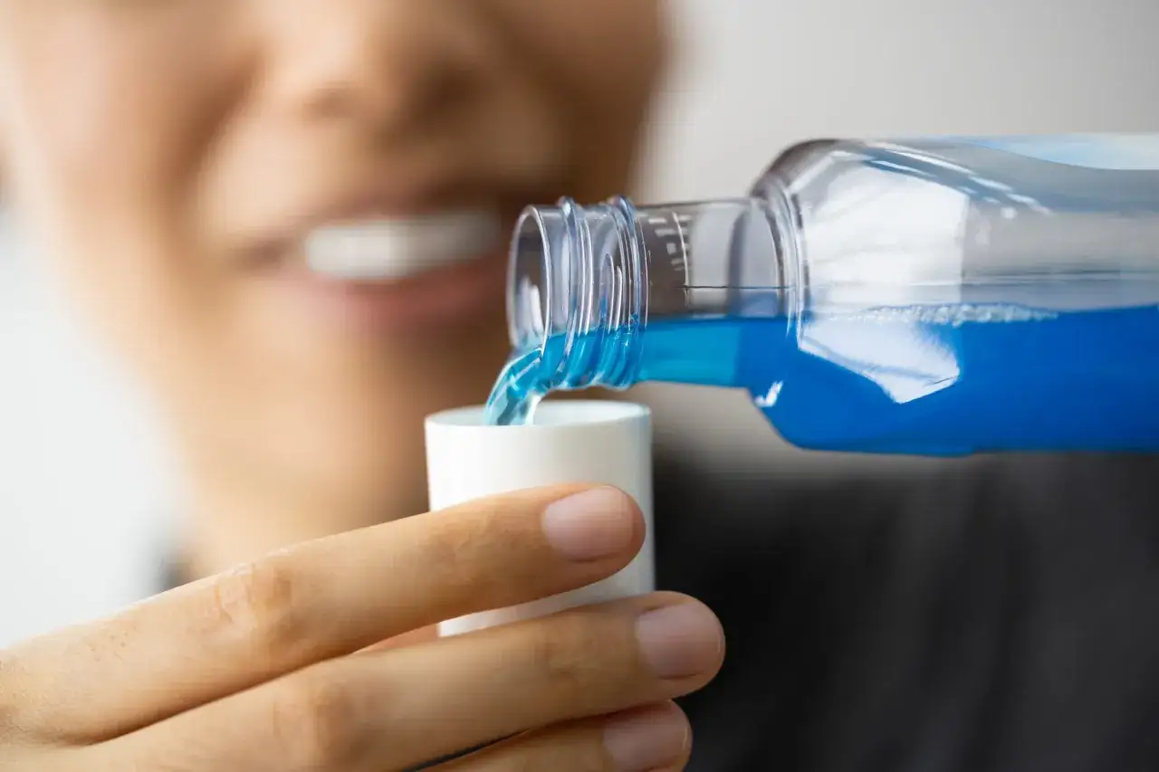 Persona versa collutorio blu nel tappo, un passo fondamentale per imparare come usare il collutorio per un sorriso smagliante.