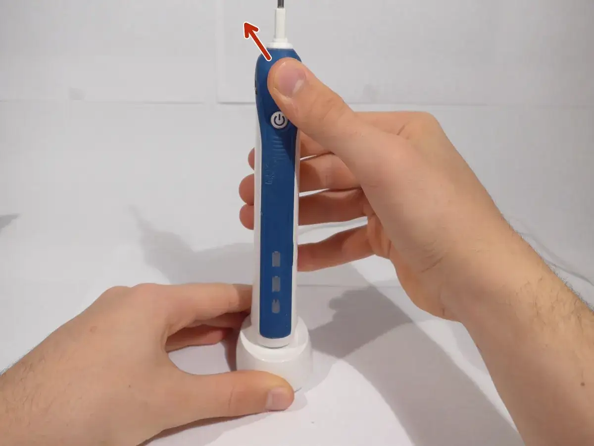 Mani che tengono uno spazzolino Oral-B blu e bianco, pronto per essere posizionato sulla base di ricarica. Per resettare spazzolino Oral-B, segui questi semplici passaggi.