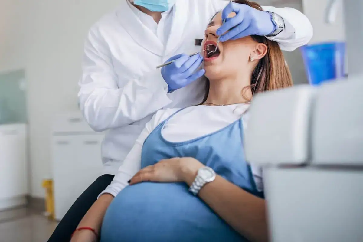 Dentista esamina la bocca di una donna incinta, sottolineando l'importanza della pulizia dei denti in gravidanza per la salute di madre e bambino.