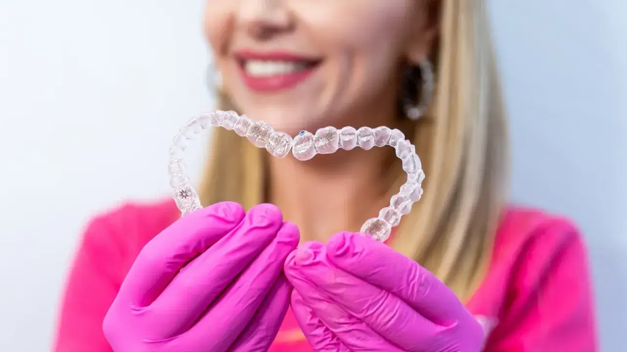 Mani guantate di rosa tengono un cuore di Invisalign, simbolo di un sorriso sano anche in gravidanza.