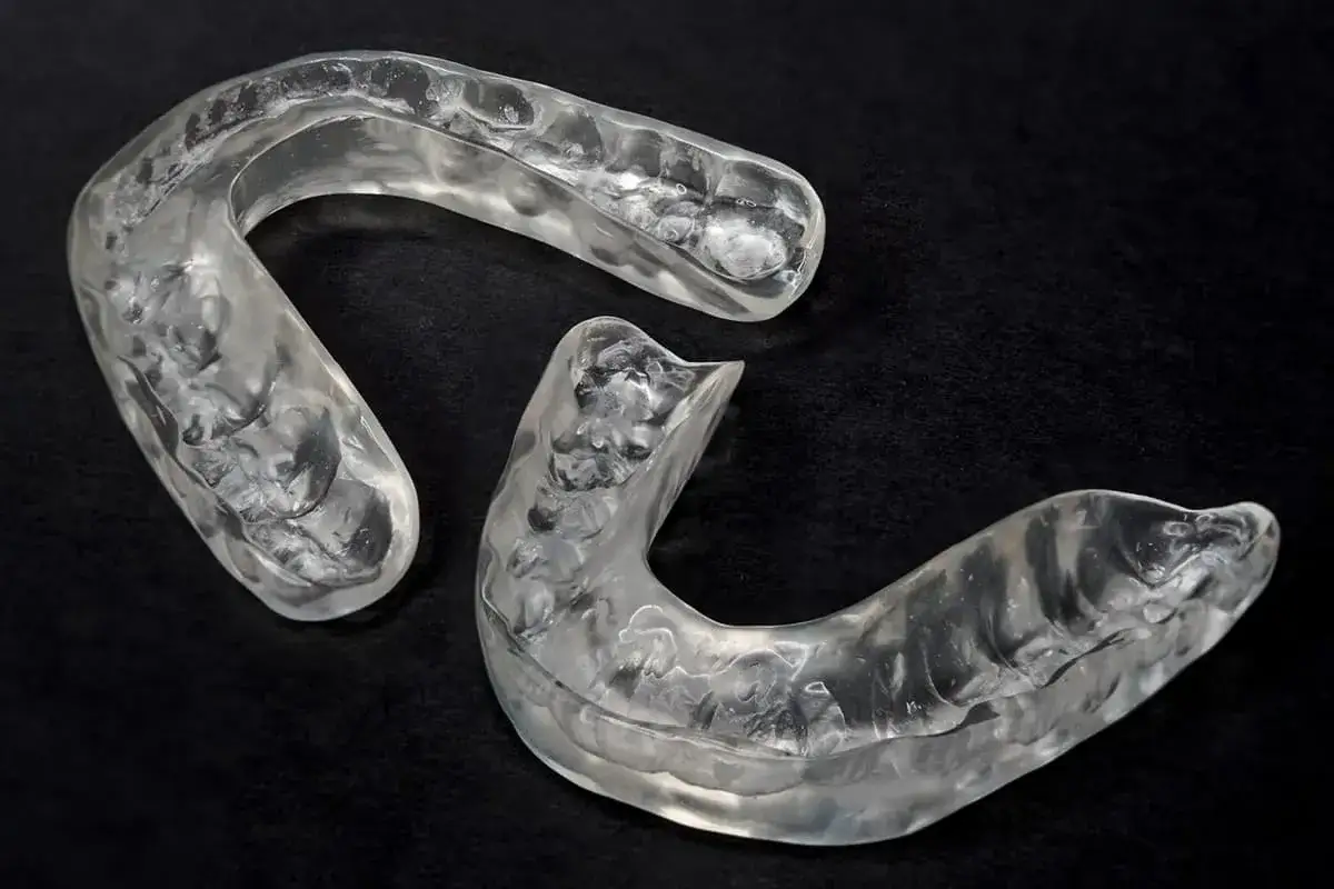 Due bite occlusali trasparenti, realizzati su misura, riposano su una superficie scura.