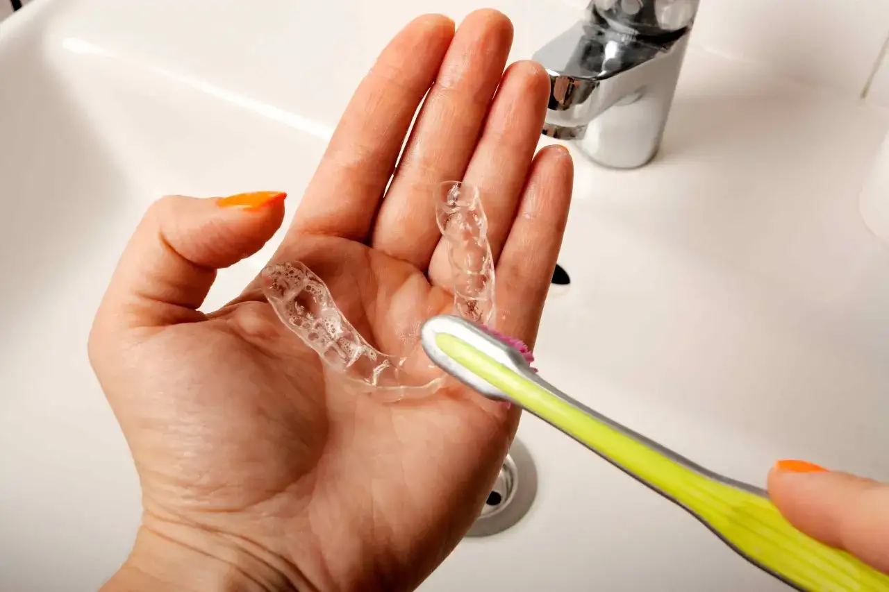 Mano che pulisce un bite trasparente con uno spazzolino, mostrando come pulire il bite per mantenerlo igienico.