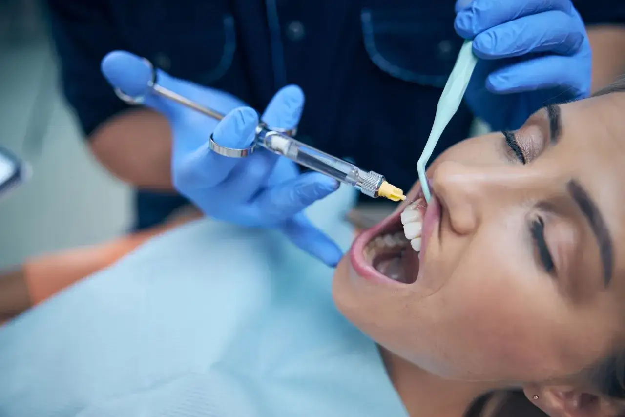 Il dentista esegue l'anestesia locale su una paziente. La siringa è tenuta da una mano guantata blu.