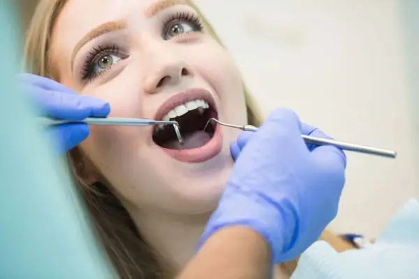 Visita dentistica: una giovane donna con un sorriso smagliante apre la bocca mentre il dentista esamina i suoi denti con strumenti, incluso uno specchietto che riflette il foro mentoniero.