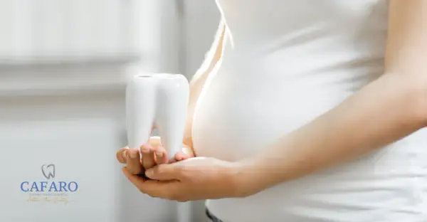 Mani di donna incinta tengono un dente bianco, simbolo della cura per la pulizia dei denti in gravidanza.