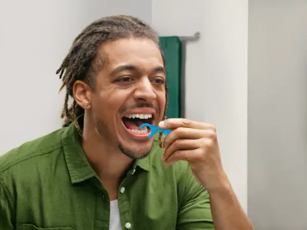 Uomo con dreadlocks usa una forcella tendifilo interdentale blu per pulire i denti.