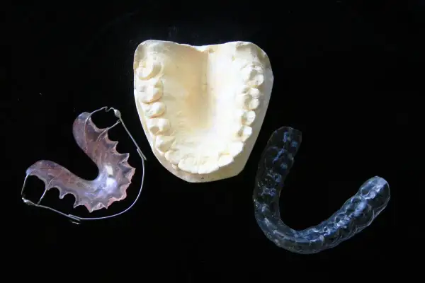 Modello dentale e apparecchi ortodontici, inclusi apparecchi invisibili per adulti, su sfondo nero.