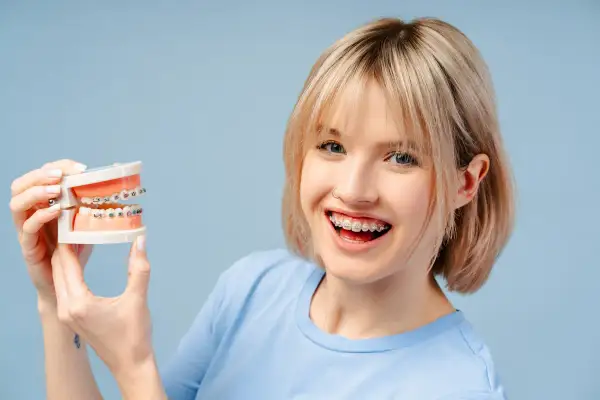 Ragazza sorridente con apparecchio dentale tiene un modello di denti. Chiediti ogni quanto si stringe l'apparecchio per un sorriso perfetto.