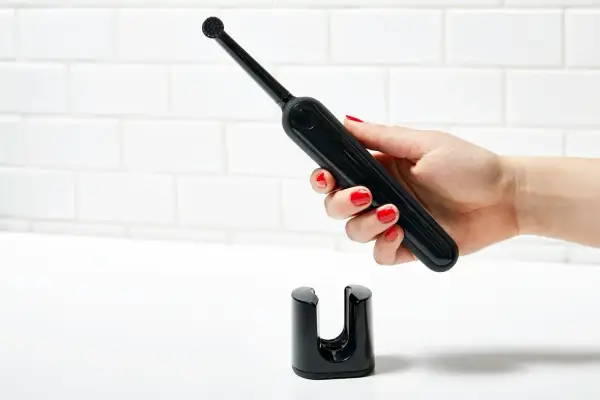 Mano con smalto rosso tiene uno spazzolino elettrico nero sopra il suo supporto. Un modo efficace per pulire muffa spazzolino elettrico.