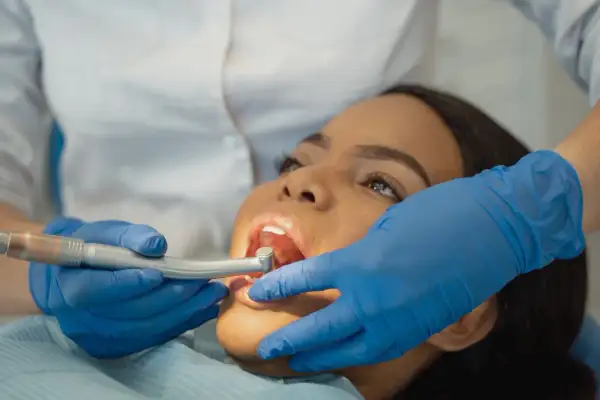 Dottoressa esegue scaling dentale su paziente. Mani con guanti blu tengono strumento odontoiatrico.