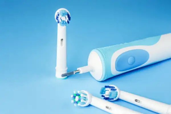Spazzolino elettrico si accende da solo, pronto per l'igiene orale. Testine di ricambio su sfondo blu.