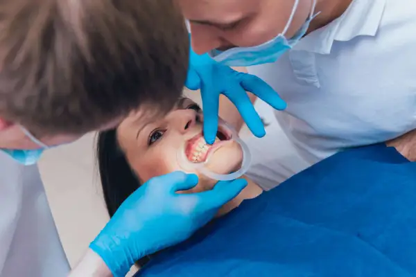 Dentista esamina i denti di una paziente, che ha un divaricatore in bocca. I mammelloni denti sono ben visibili.